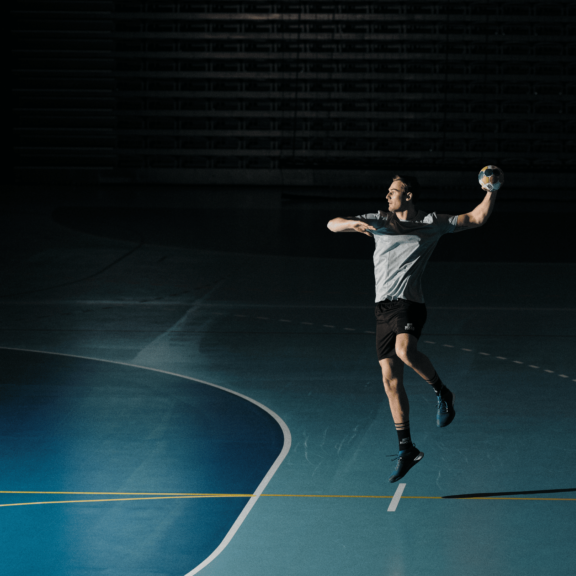 Handballspieler wirft Ball in einer leeren Sporthalle.