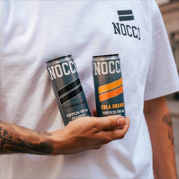 Person hält zwei Dosen NOCCO Energydrinks in den Händen.
