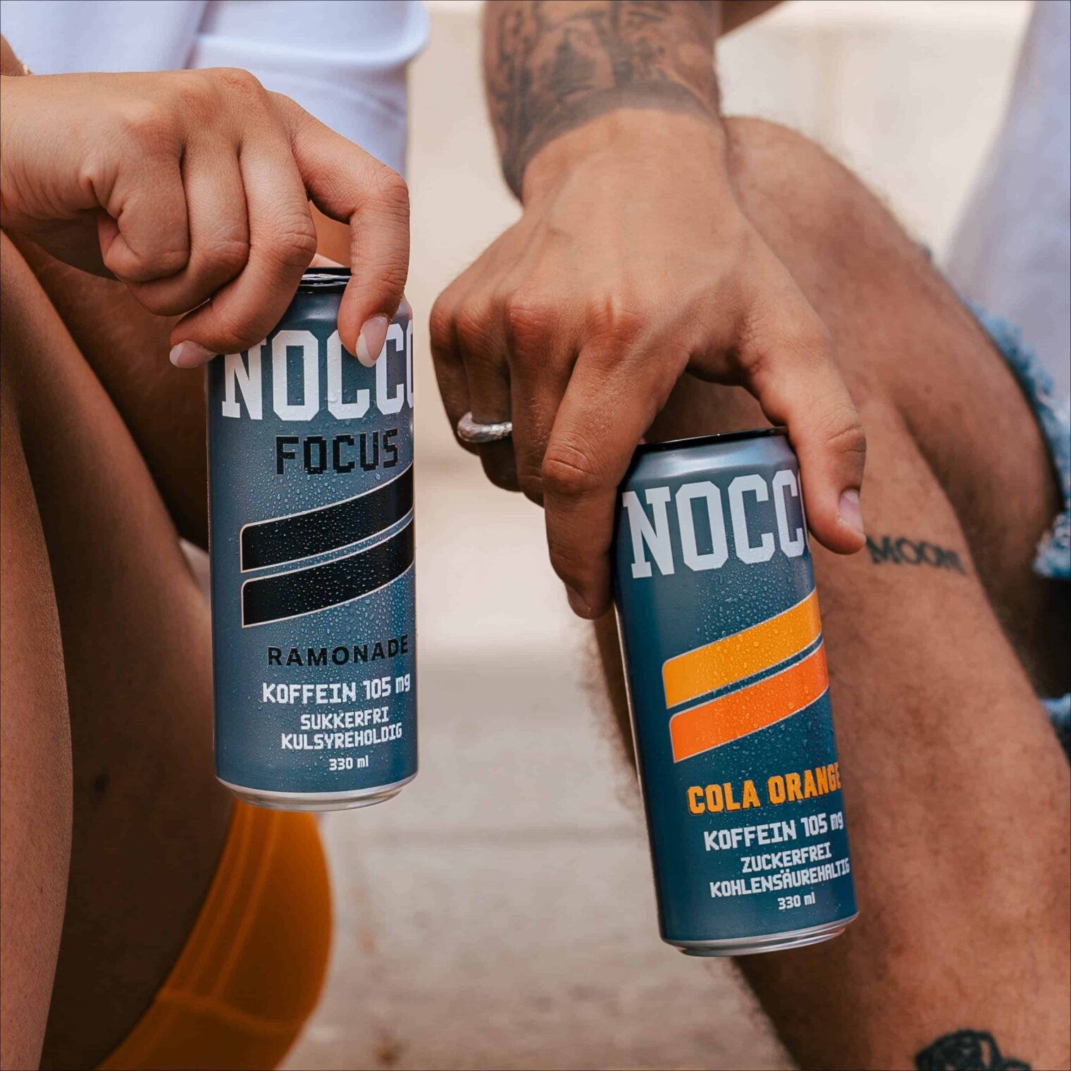 Zwei Personen halten Dosen mit Energydrinks, eine mit Zitrone-, die andere mit Cola-Orangen-Geschmack.