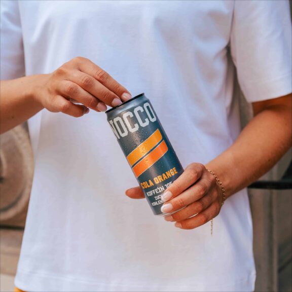 Person hält eine Dose NOCCO Cola Orange.